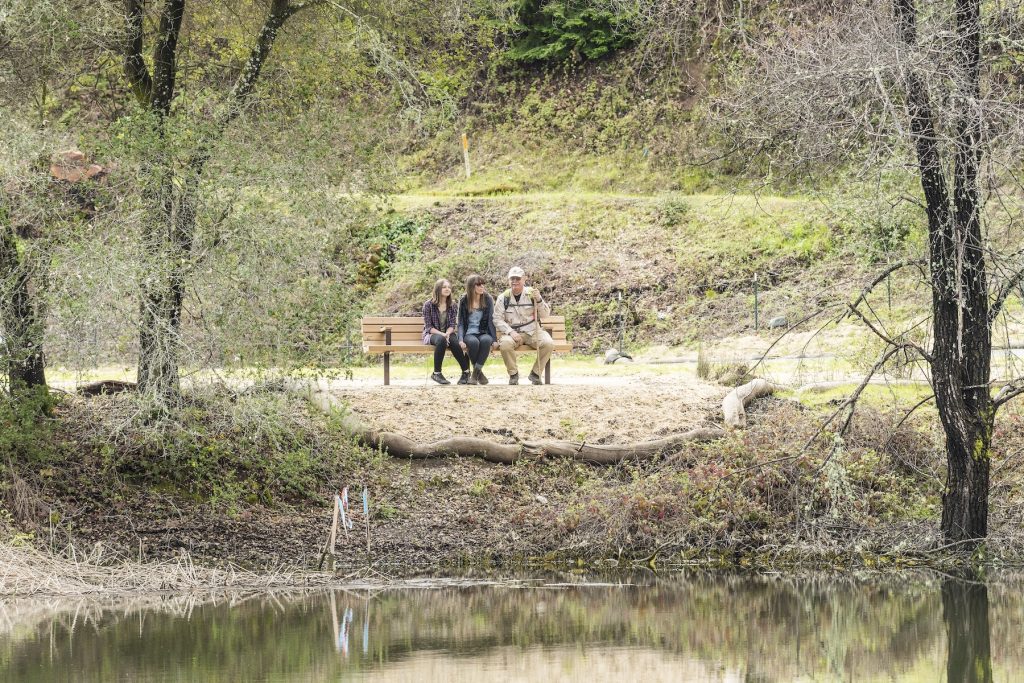 Folks sit on bench beside creek