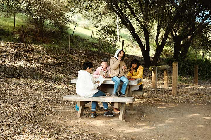 A family enjoys time together at a picnic table in the shade.